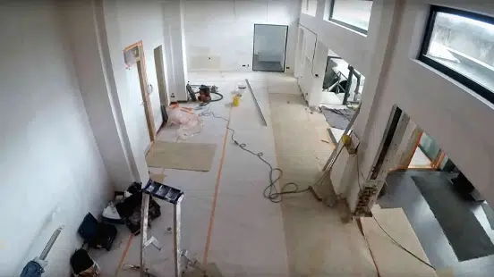 Vue en angle élevé du showroom de D&O Partners au cours de son relooking, avec des matériaux de construction éparpillés, des murs partiellement finis et des fenêtres hautes laissant entrer la lumière naturelle.