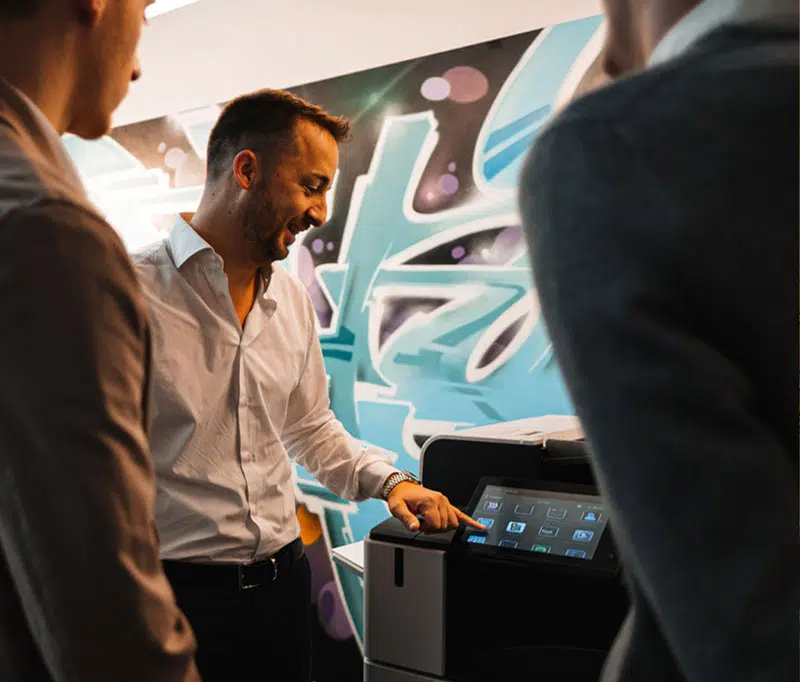 Un professionnel de la vente souriant effectue une démonstration interactive sur l'écran tactile d'une imprimante Xerox chez D&O Partners, illustrant l'engagement de plus de 20 ans de la société à fournir des services Xerox dédiés.