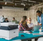 Xerox C315 colour printer on a meeting table in a busy office, used by professionals working together efficiently, supplied by D&O Partners.