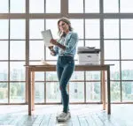 Imprimante monochrome Xerox B305 posée à côté d'une femme souriante en milieu professionnel, illustrant la facilité d'usage et la qualité d'impression pour les professionnels, disponible via D&O Partners.