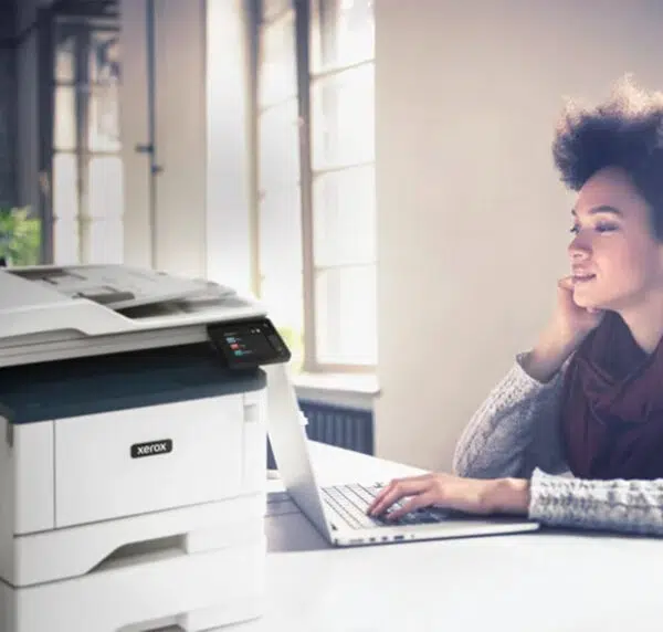 Woman working from home with a Xerox B315 multifunction printer, supplied by D&O Partners, illustrating harmonious integration into a home workspace.