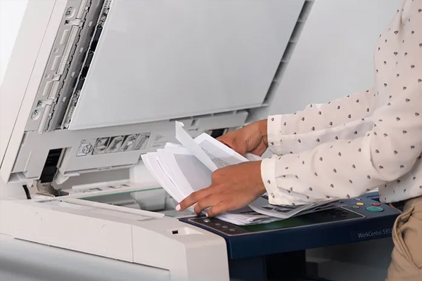 Une personne en train d’organiser des documents pour la copie ou l’impression sur une machine Xerox, représentant les solutions de gestion documentaire fournies par D&O Partners.