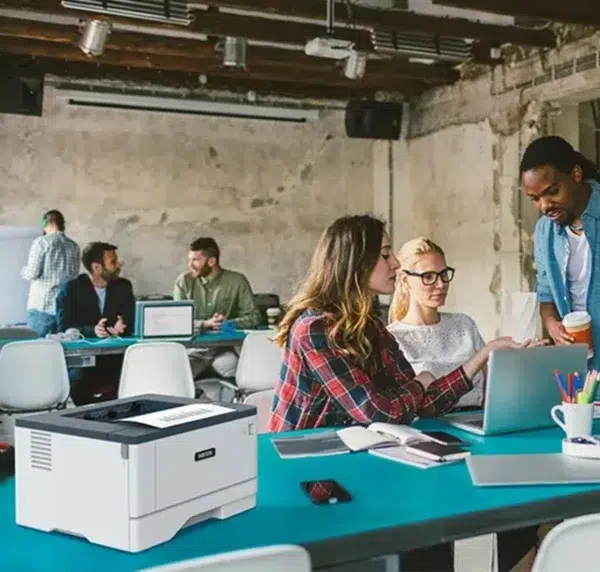 Xerox B310 monochrome printer on a meeting table in a busy office, used by professionals working together effectively, supplied by D&O Partners.