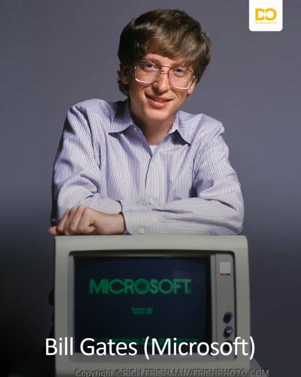 Young Bill Gates leaning on a computer displaying the Microsoft logo