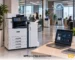 Imprimante multifonction A3 Xerox dans un environnement de bureau, connectée à un tableau de bord Managed Print Services pour la gestion centralisée du parc.